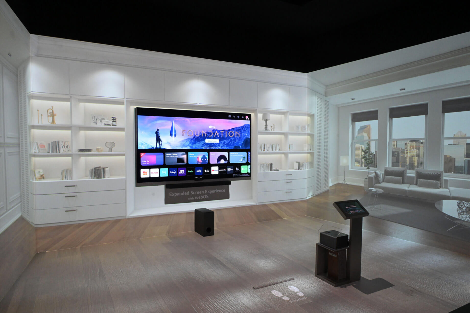 Der 97" große LG Signature OLED M3 TV steht in einem großen Raum an der Wand. Die schwarze Zero-Connct-Box befindet sich in der Mitte vom Raum und übertrage das Audio- und Videosignal kabellos zum TV